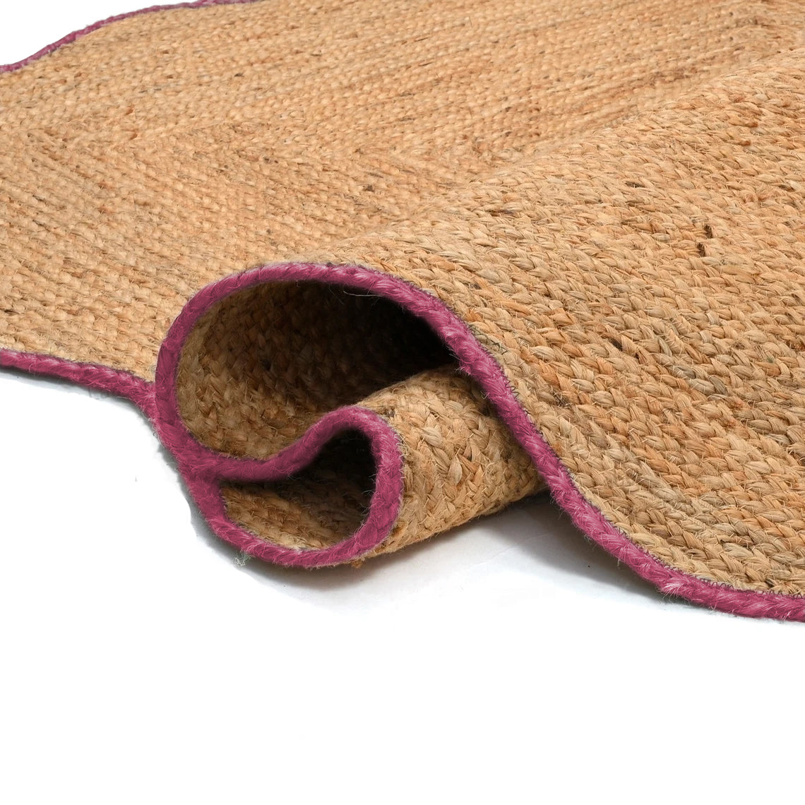 Handwoven natural jute scalloped area rug with pink border placed in a modern living room featuring a charcoal grey sofa.