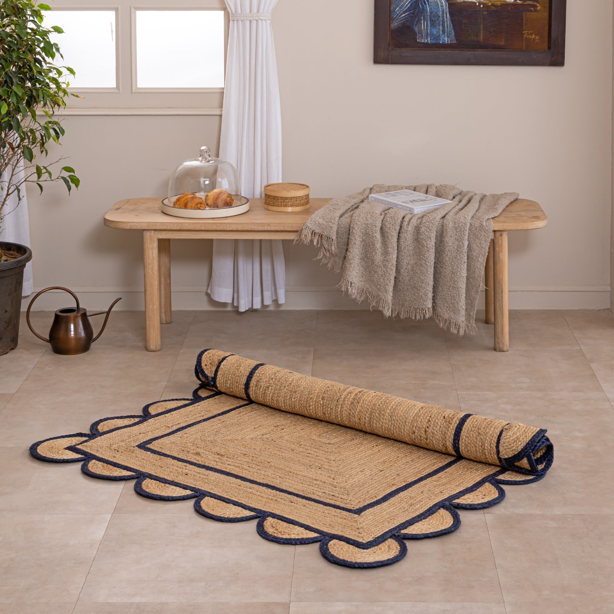 Handmade natural jute area rug with navy blue scalloped braided border in a cozy modern living room.