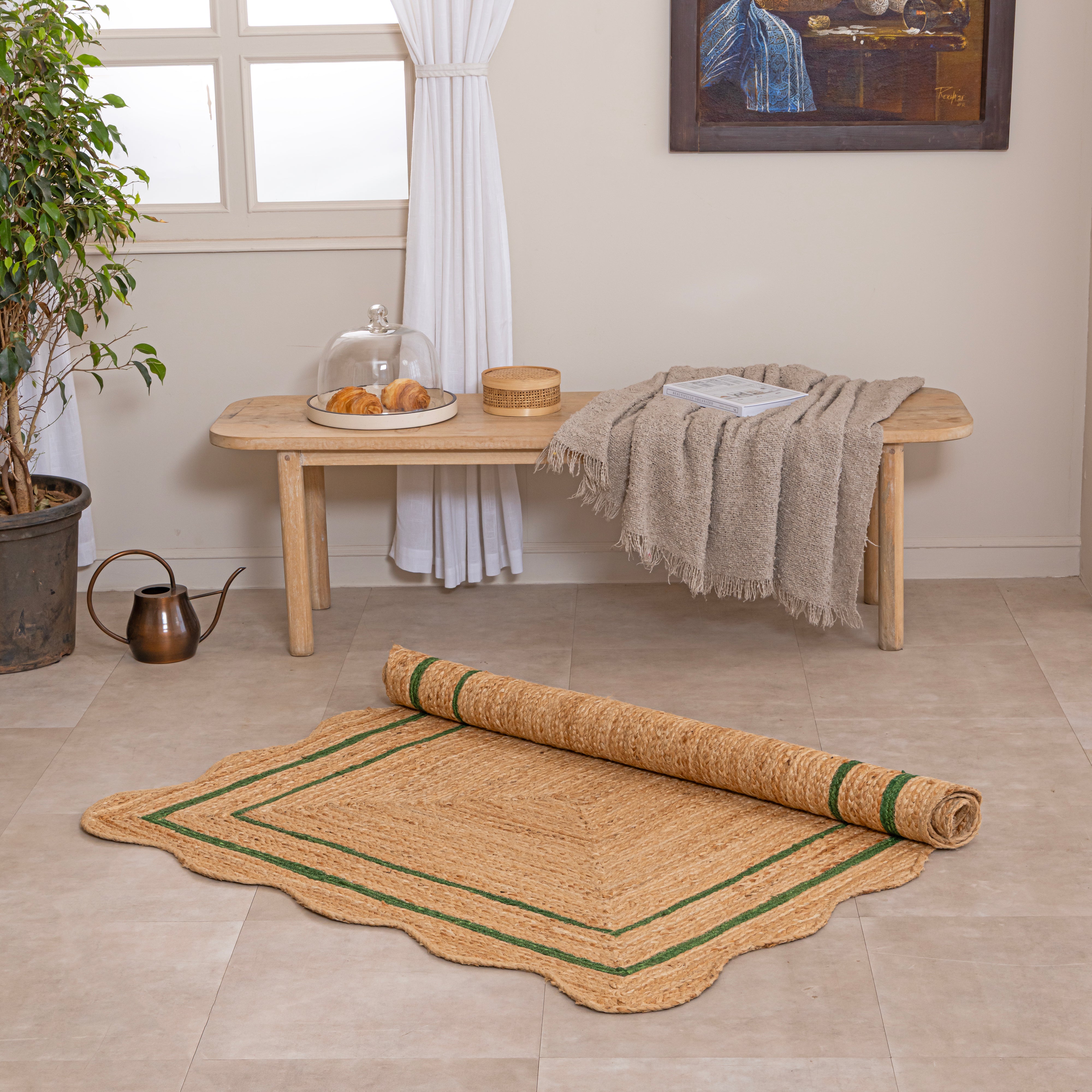 Handwoven natural jute area rug with green double border, styled in a cozy modern living room with neutral home decor.