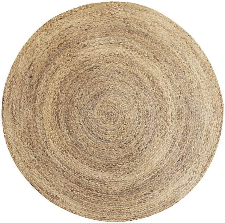 A handwoven, round natural jute area rug placed on a light wood floor in a cozy, brightly lit modern living room with a beige sofa and woven decor.