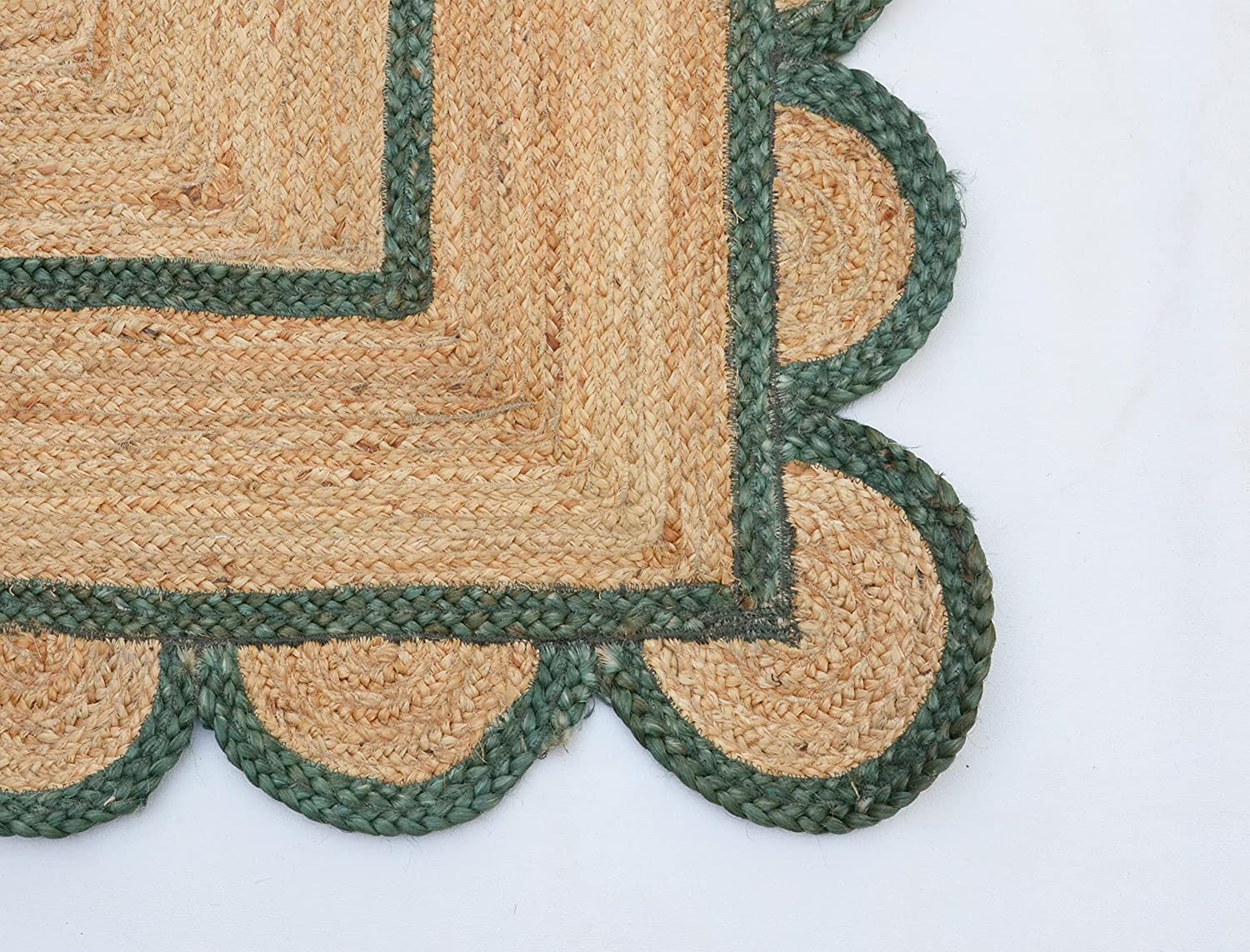 Handwoven natural jute area rug with green scalloped border placed in a modern Scandinavian living room featuring sustainable eco-friendly braided craftsmanship.