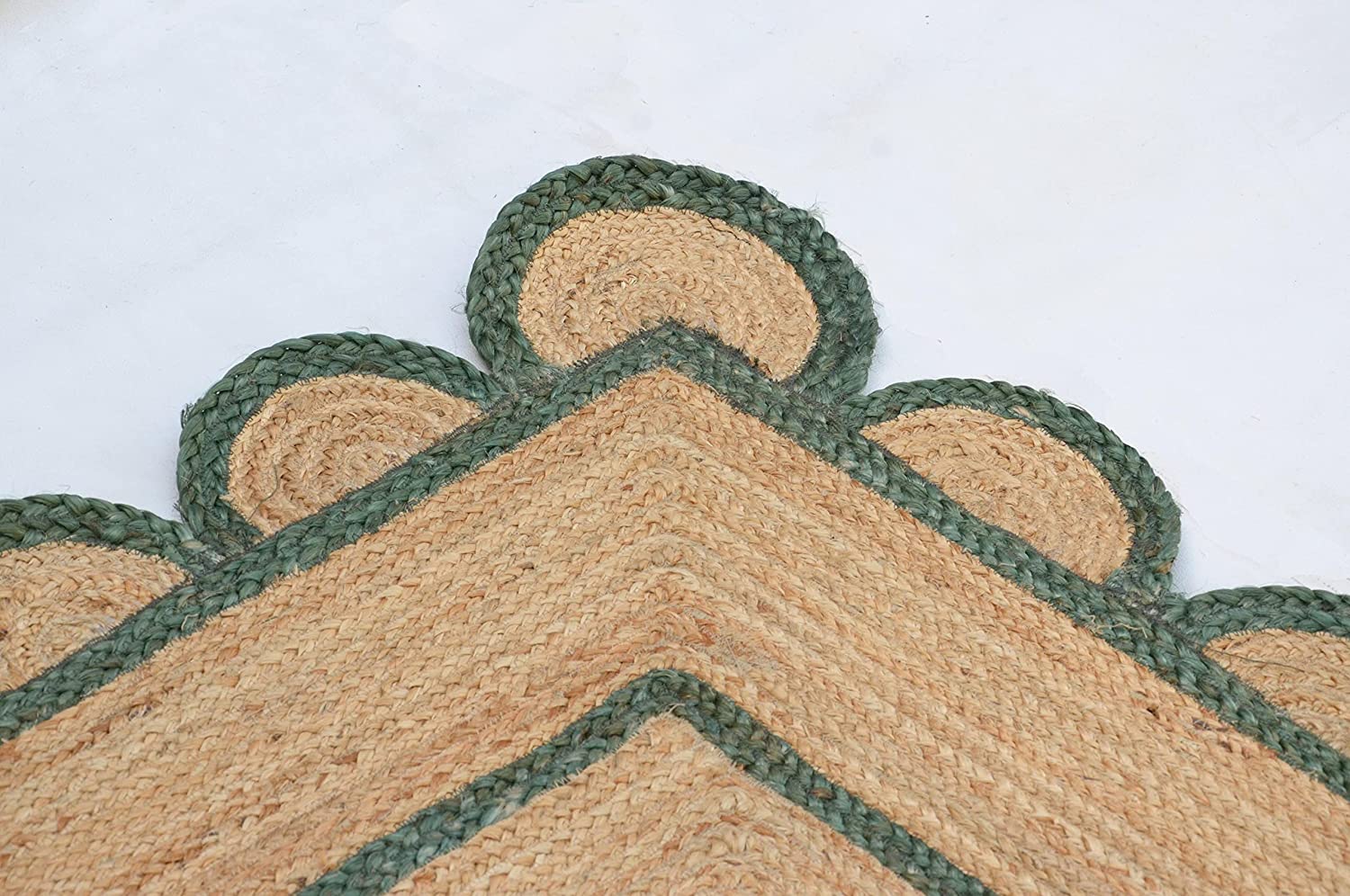Handwoven natural jute area rug with green scalloped border placed in a modern Scandinavian living room featuring sustainable eco-friendly braided craftsmanship.