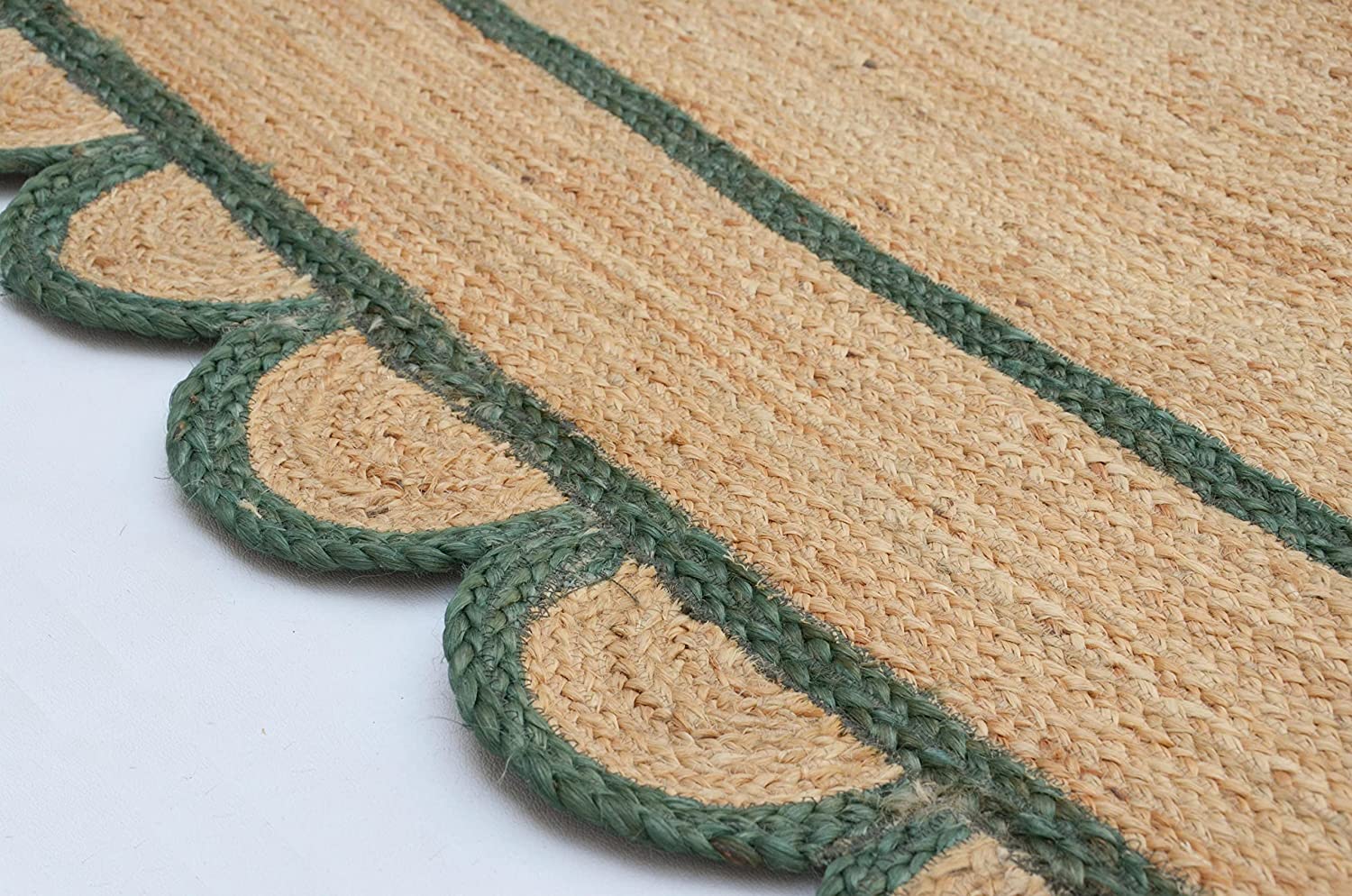Handwoven natural jute area rug with green scalloped border placed in a modern Scandinavian living room featuring sustainable eco-friendly braided craftsmanship.