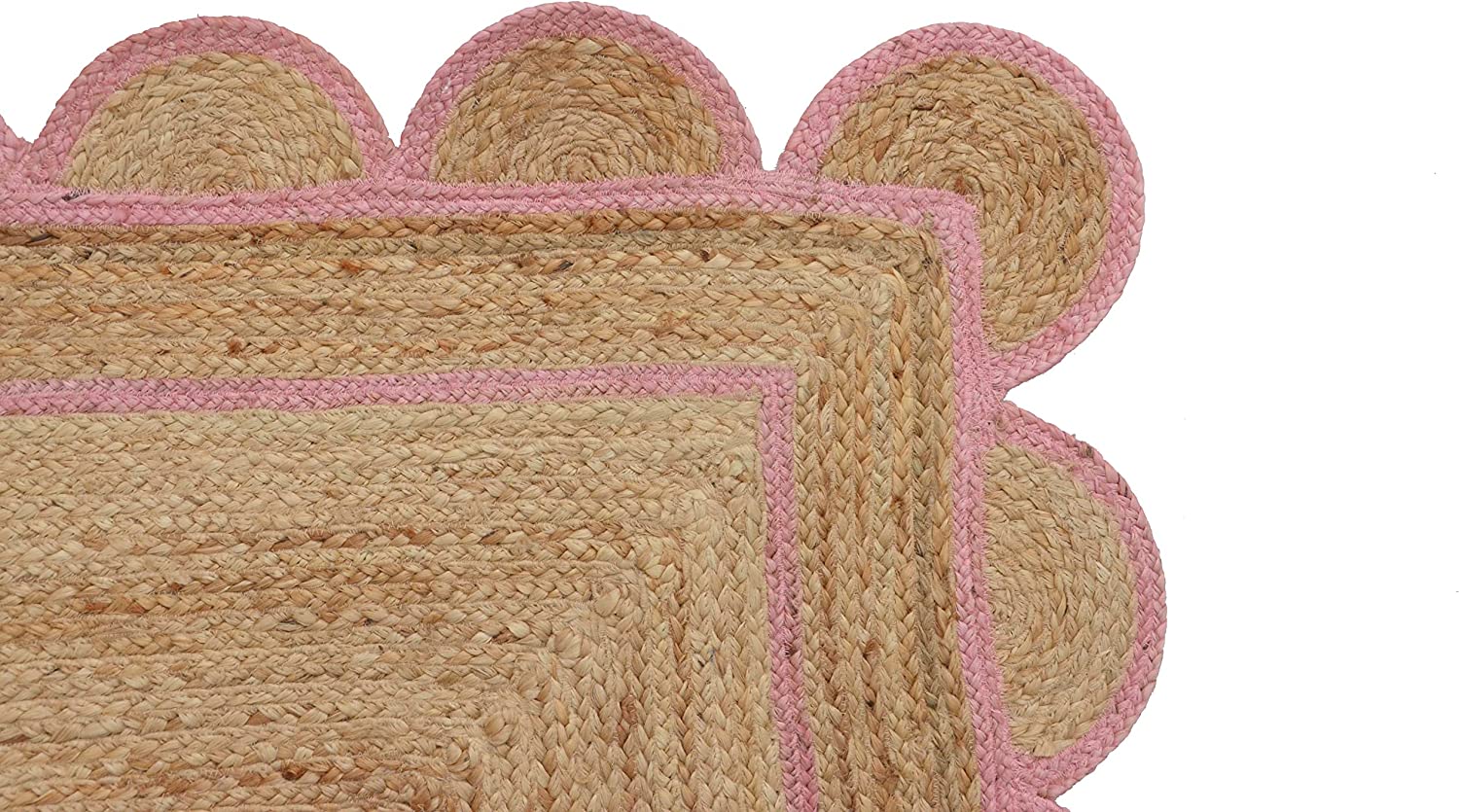 Handwoven natural jute area rug with soft pink scalloped border styled in a modern Scandinavian living room with cream sofa and wooden flooring.