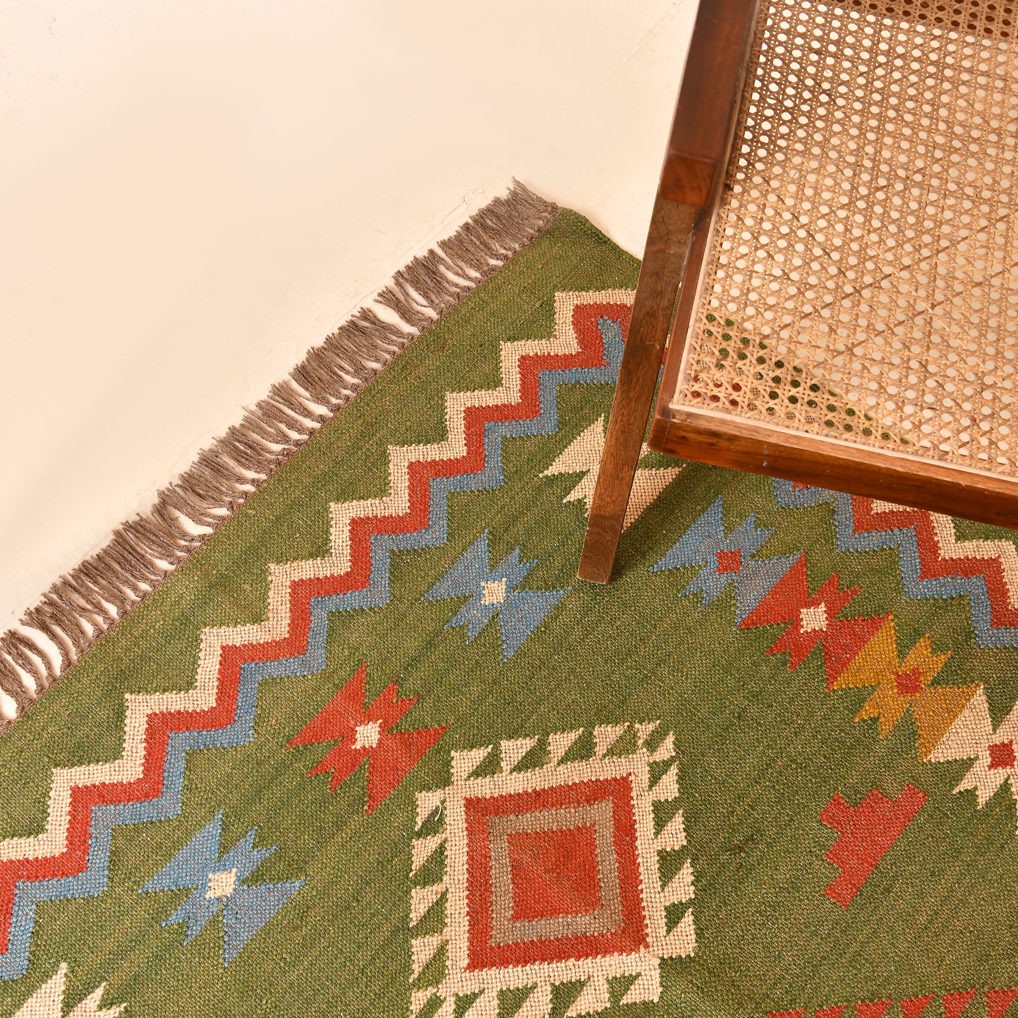 Handwoven Green Kilim Area Rug with colorful tribal geometric pattern made from wool and cotton, styled in a modern living room with wooden chair and side table.