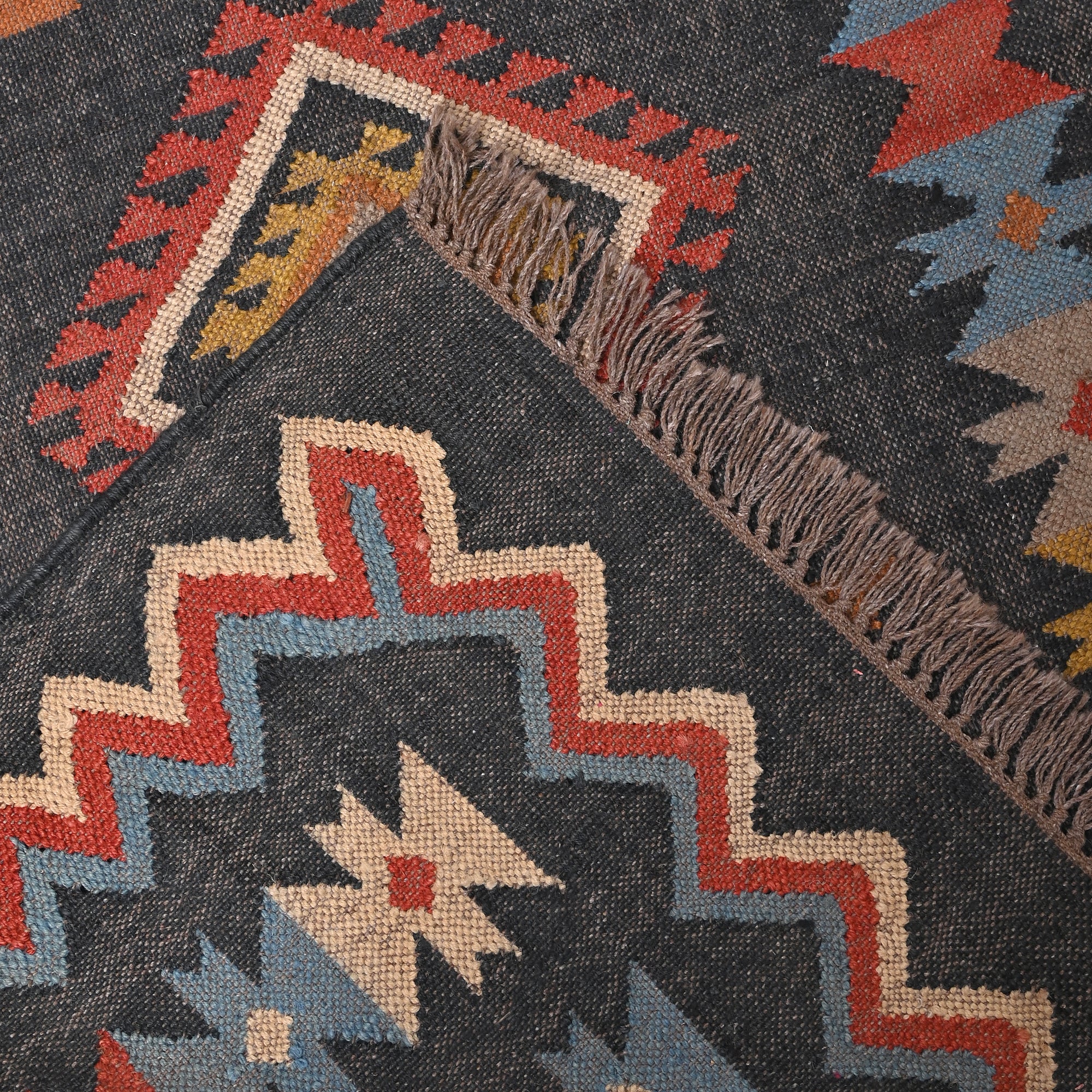Handwoven charcoal grey wool and jute Southwestern tribal flatweave area rug with colorful geometric pattern.