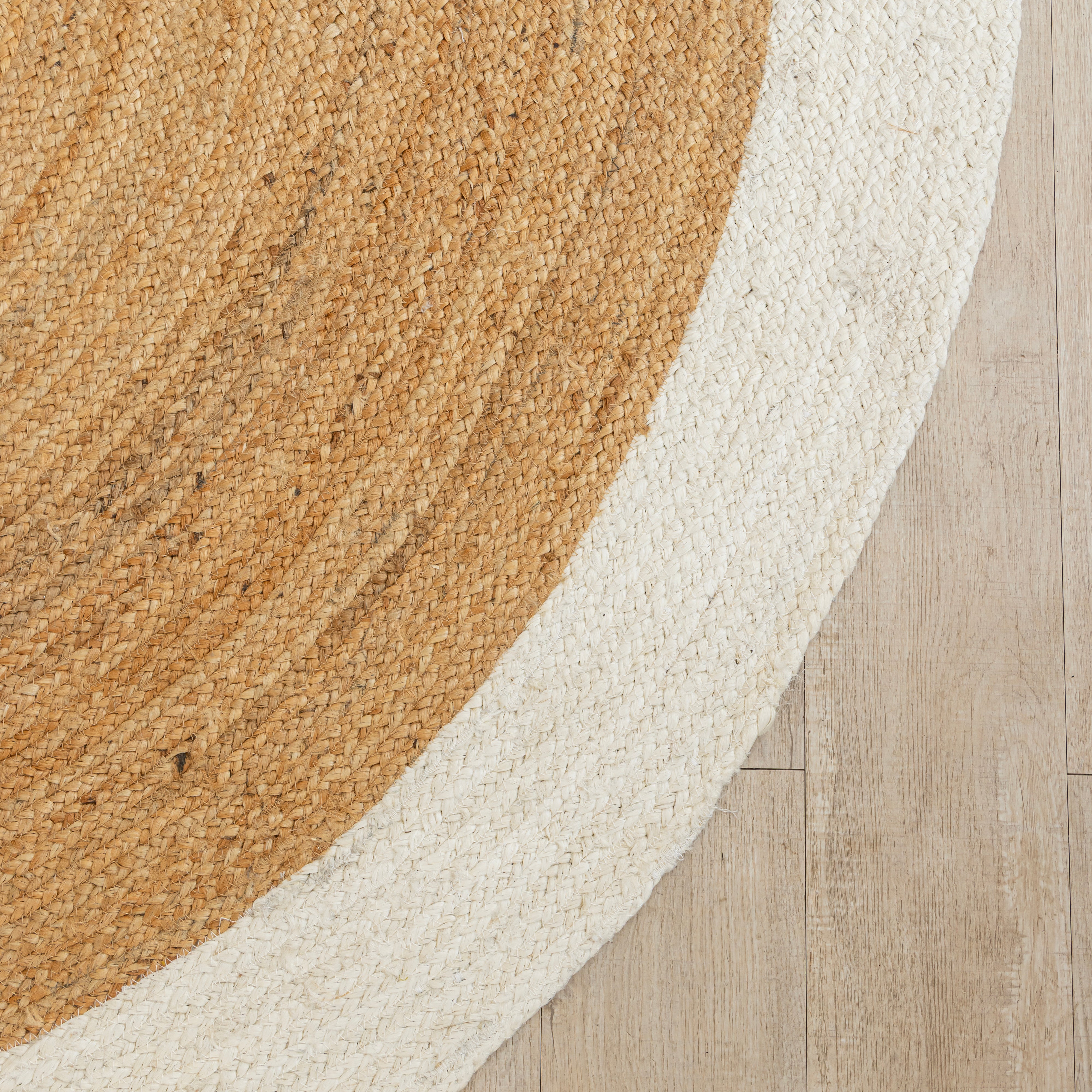 Handwoven round natural jute rug with white border placed in a modern living room featuring a wooden chair and minimalist home décor.