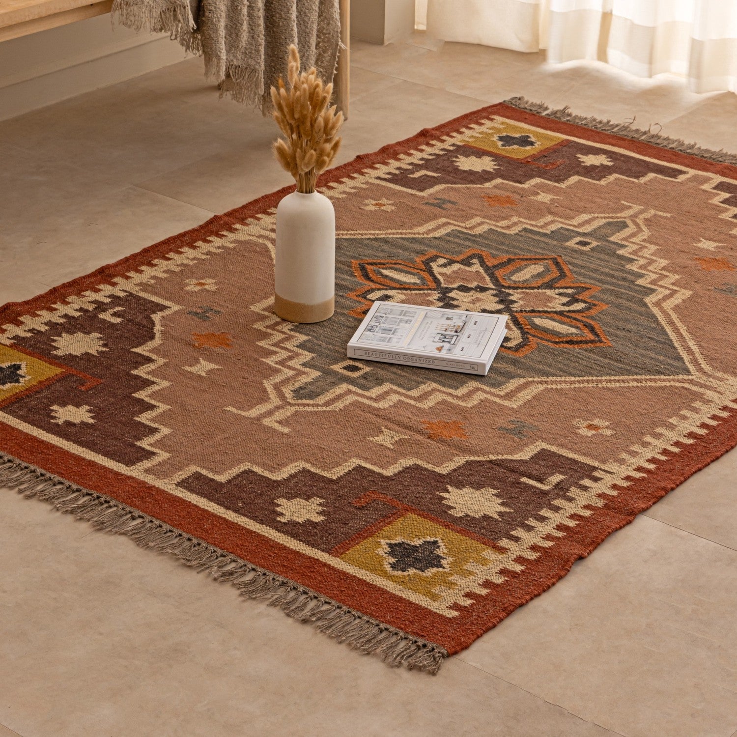 Handmade geometric tribal area rug in rust brown, beige and mustard tones with fringed edges, styled in a cozy modern living room.