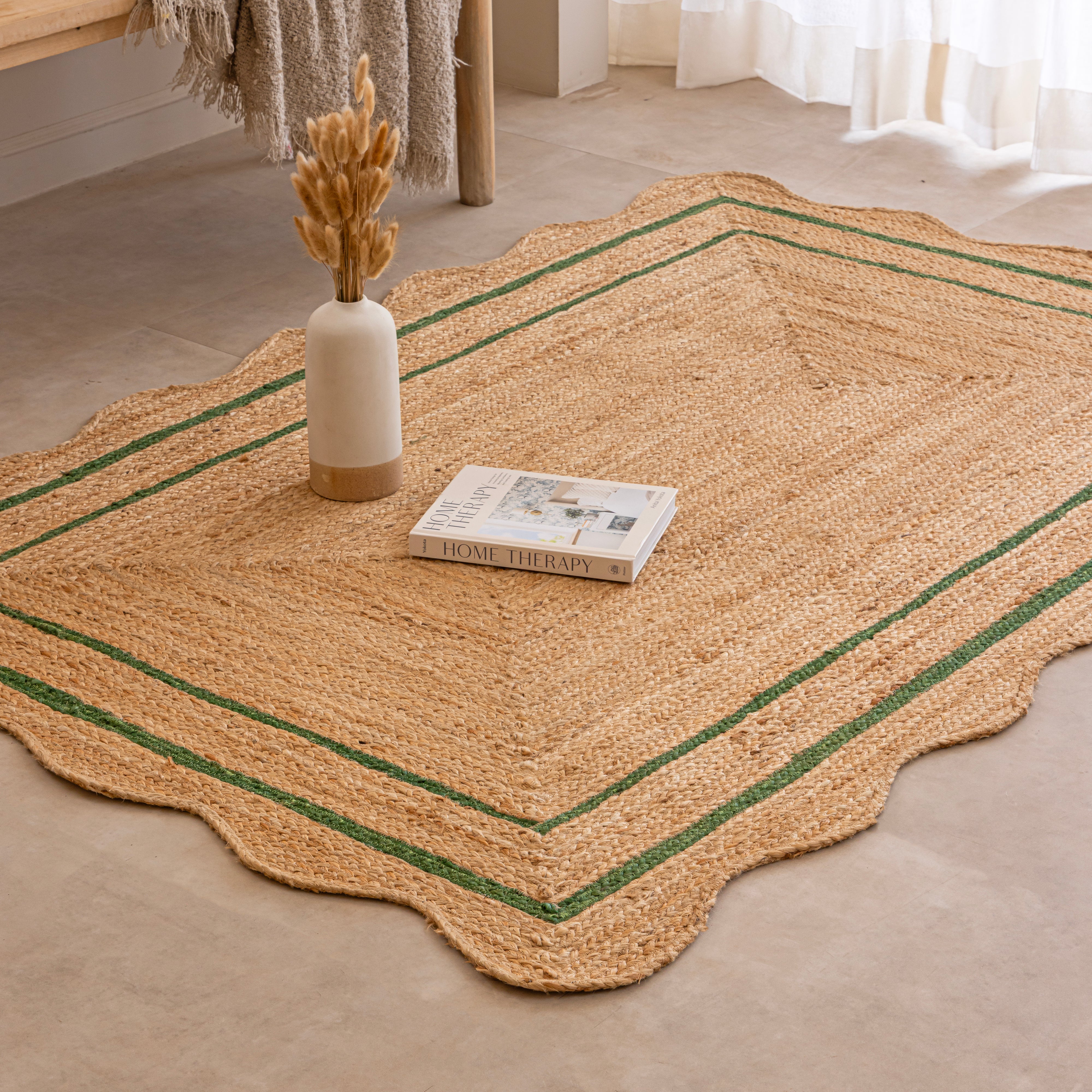 Handwoven natural jute area rug with green double border, styled in a cozy modern living room with neutral home decor.
