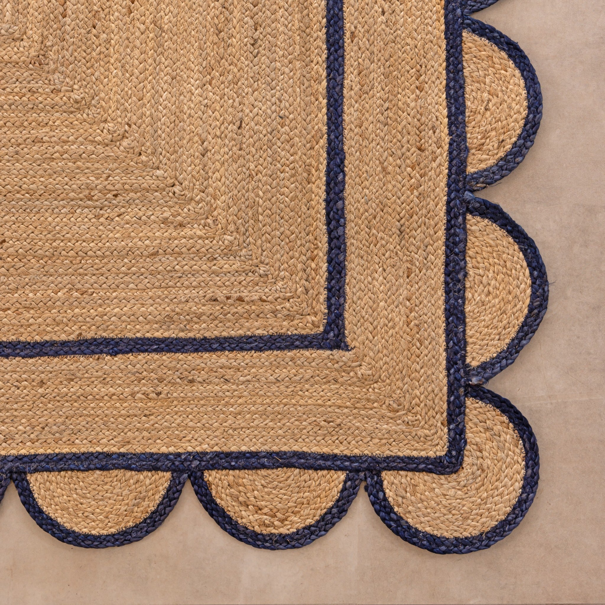 Handmade natural jute area rug with navy blue scalloped braided border in a cozy modern living room.