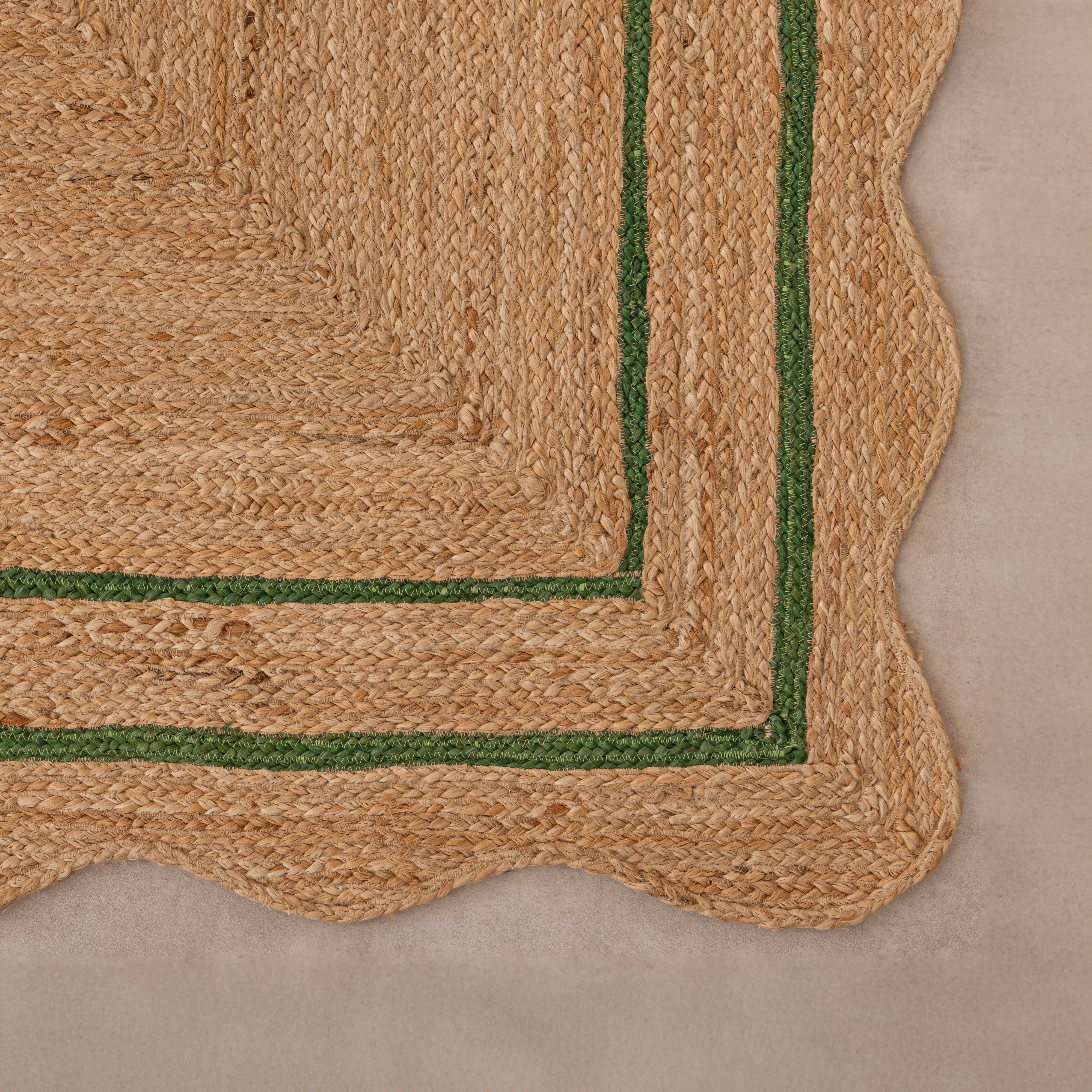 Handwoven natural jute area rug with green double border, styled in a cozy modern living room with neutral home decor.