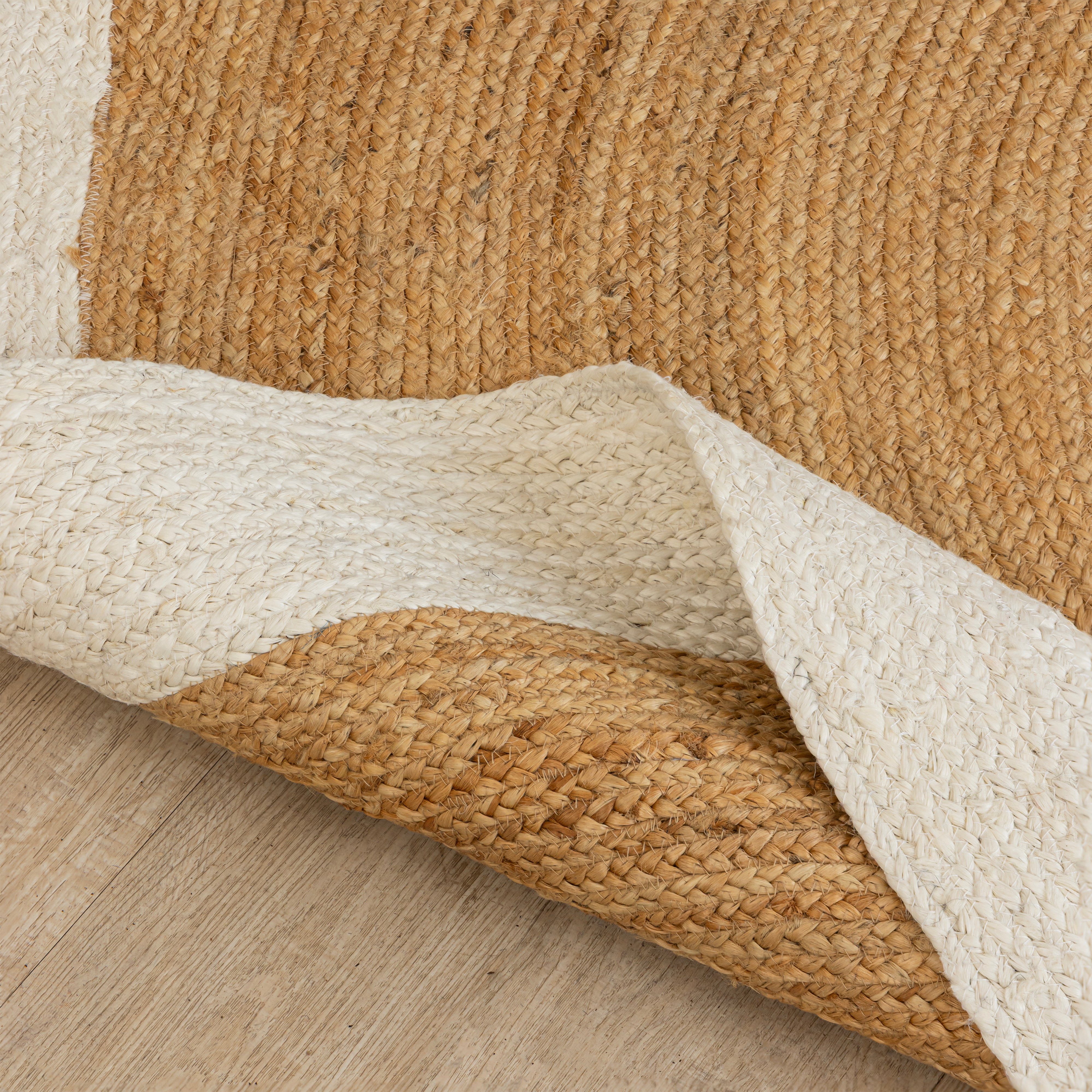 Handwoven round natural jute rug with white border placed in a modern living room featuring a wooden chair and minimalist home décor.