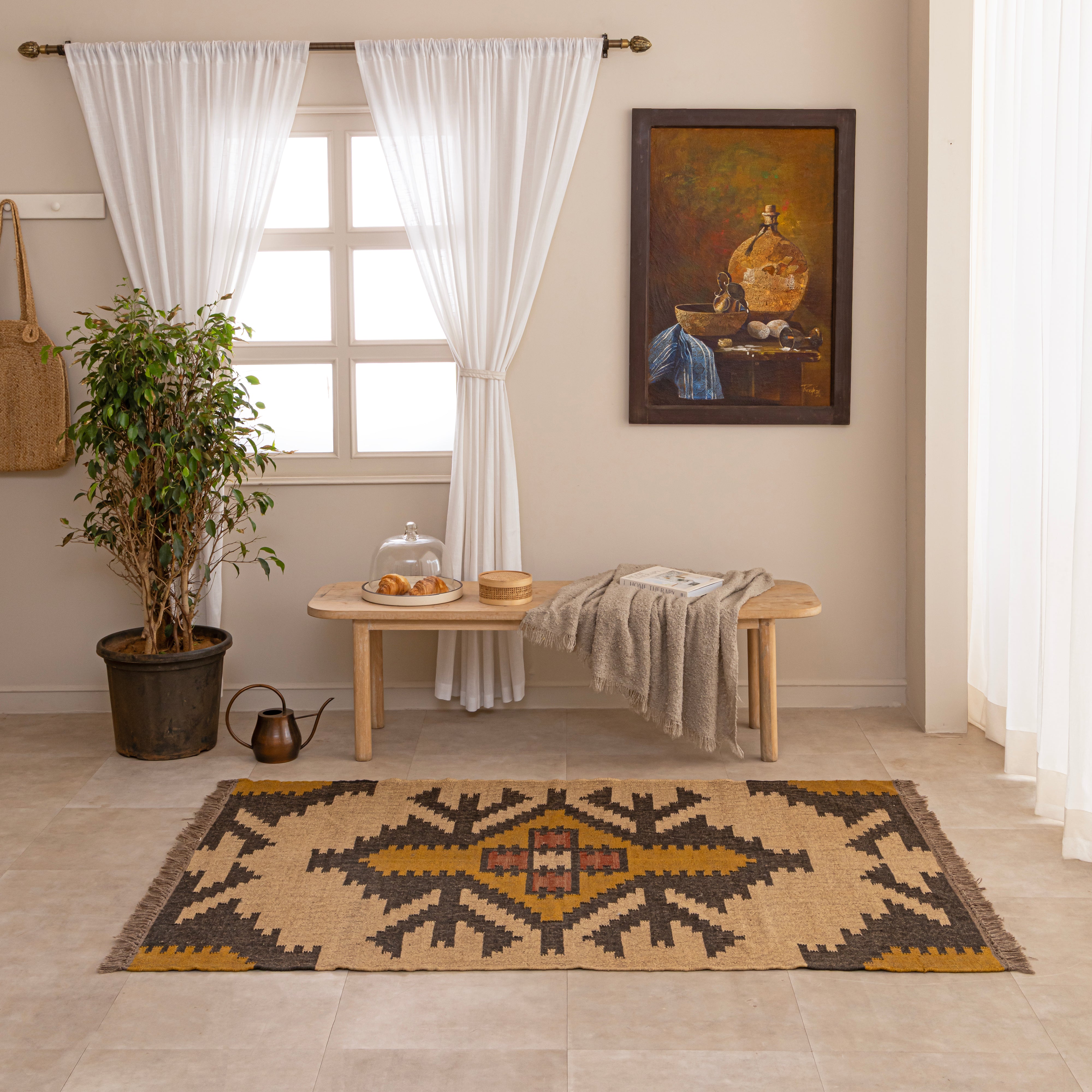Handwoven Southwestern style natural jute kilim rug with geometric black and yellow patterns and fringed edges, styled on a beige tiled floor in front of a wooden bench and large indoor plant.