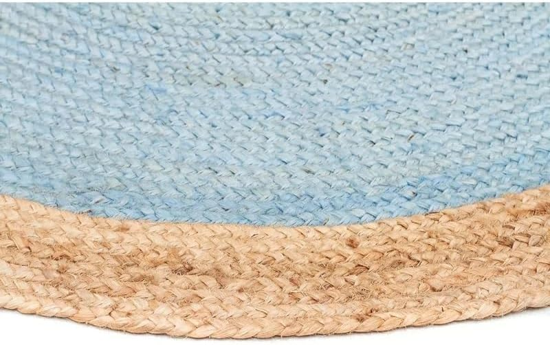 A two-tone round jute area rug featuring a muted light blue braided center and a natural tan woven border, laid on a light wood floor in a cozy coastal living room.