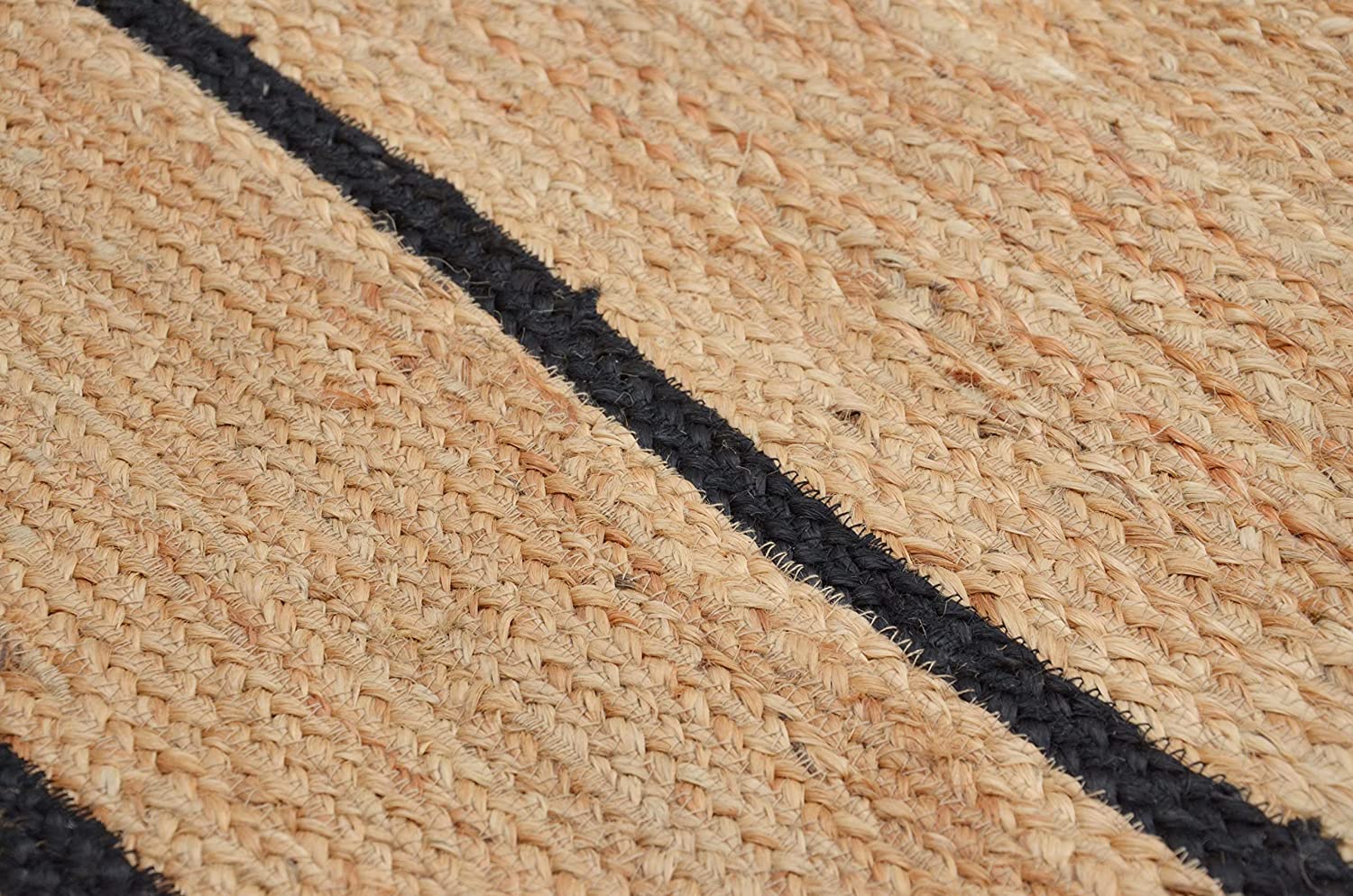 Handwoven natural jute area rug with black scalloped border in a modern Scandinavian living room featuring a cream sofa, wooden chair, and light wood flooring.