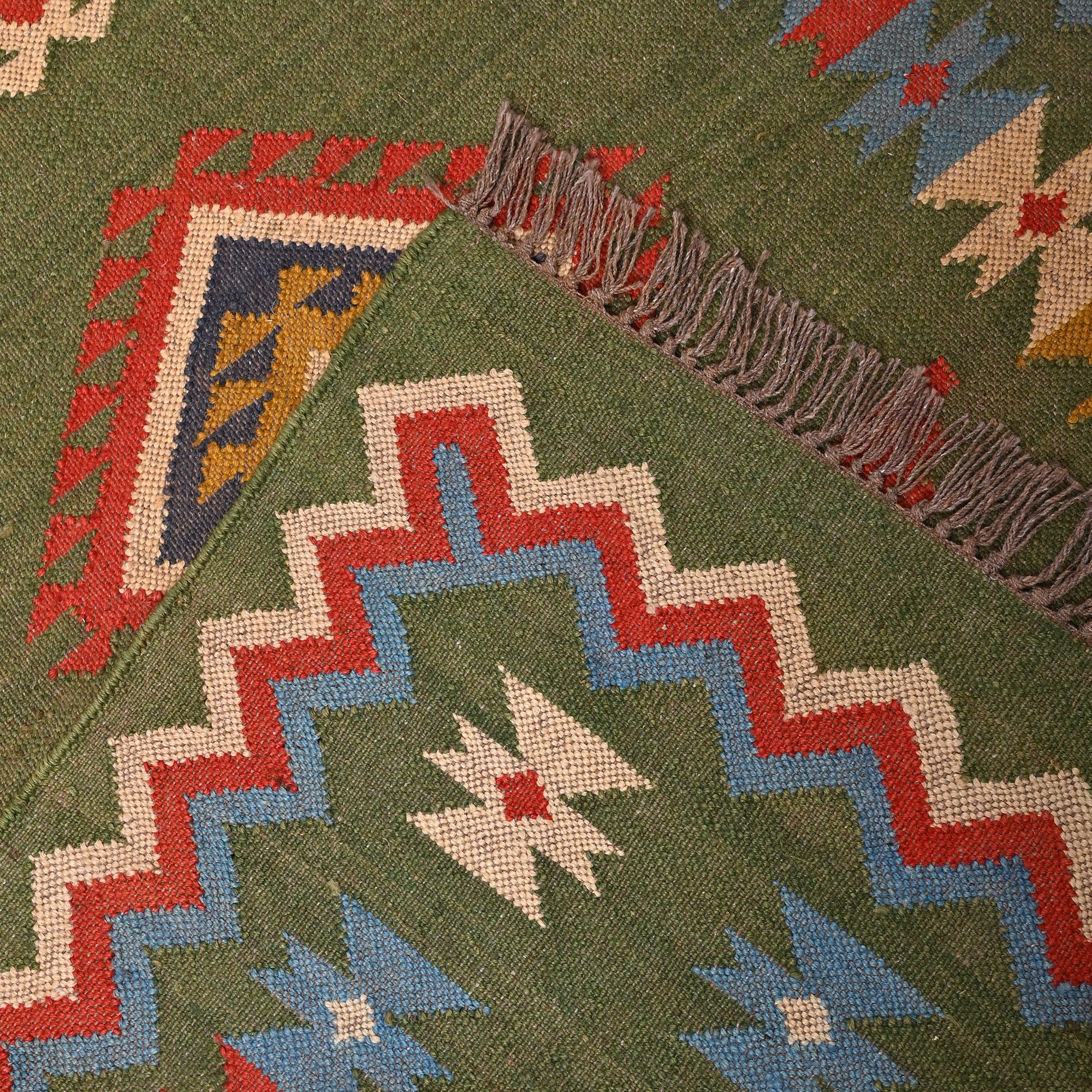 Handwoven Green Kilim Area Rug with colorful tribal geometric pattern made from wool and cotton, styled in a modern living room with wooden chair and side table.