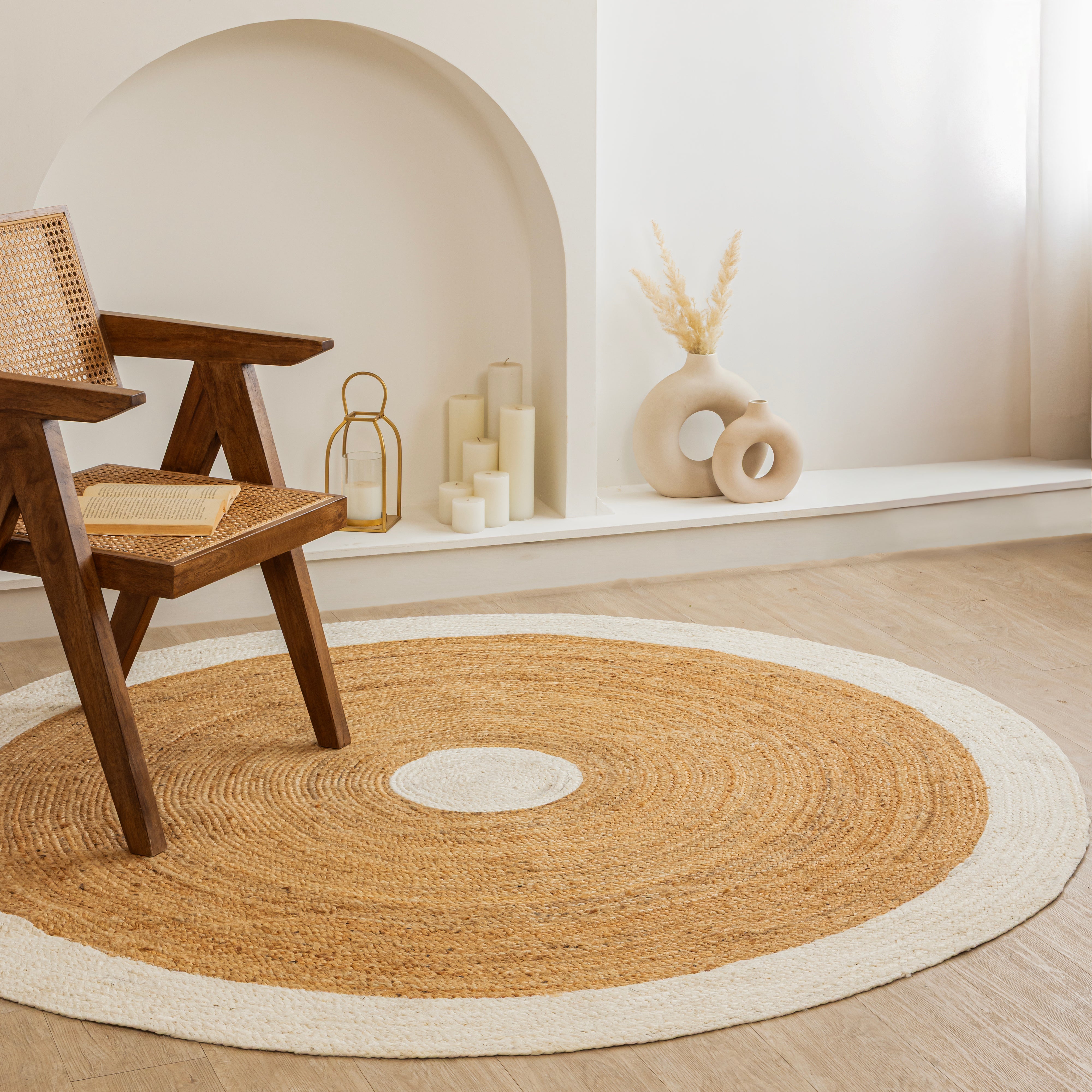 Handwoven round natural jute rug with white border placed in a modern living room featuring a wooden chair and minimalist home décor.