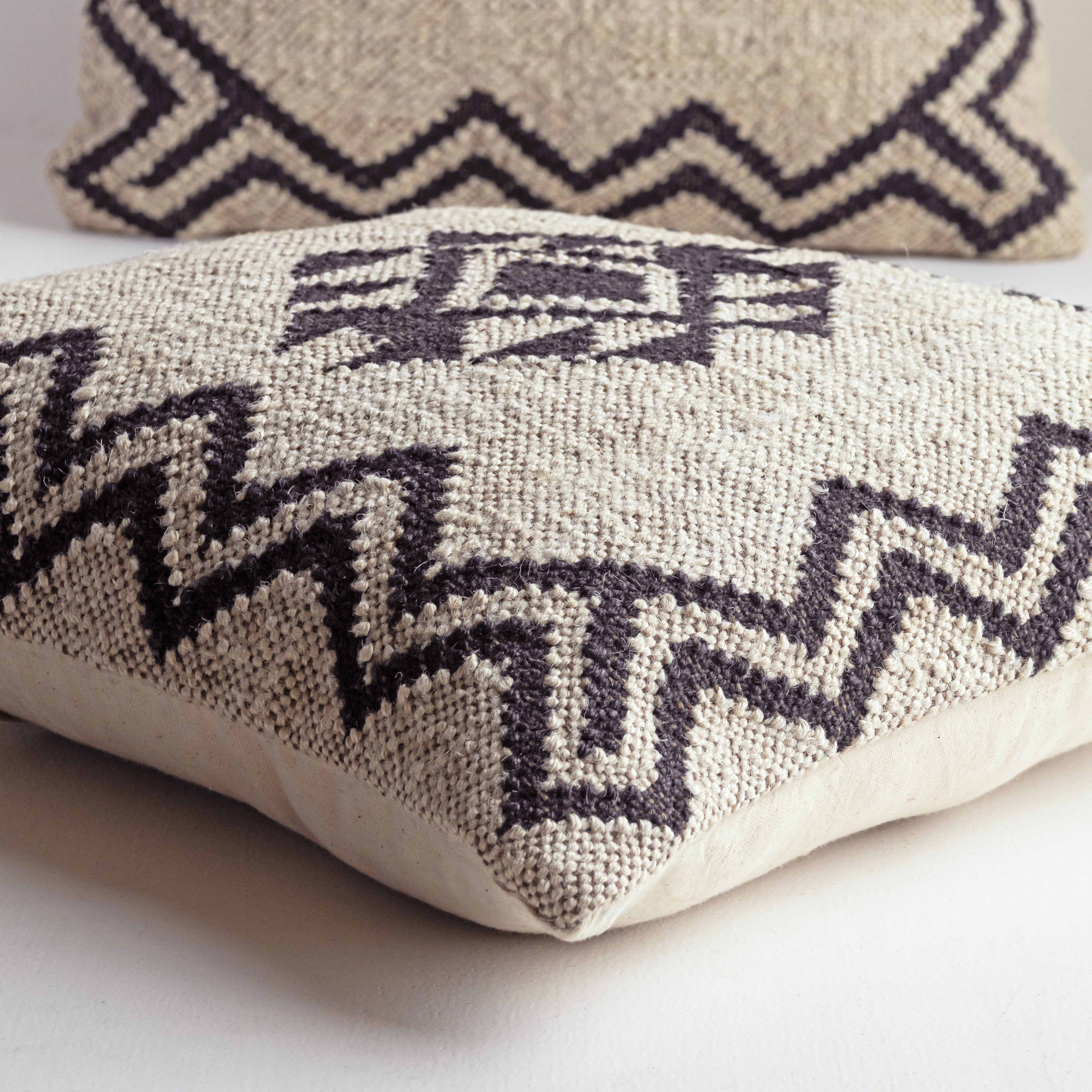 Handwoven black and ivory Kilim cushion cover featuring a geometric tribal diamond pattern displayed in a modern minimalist home setting.
