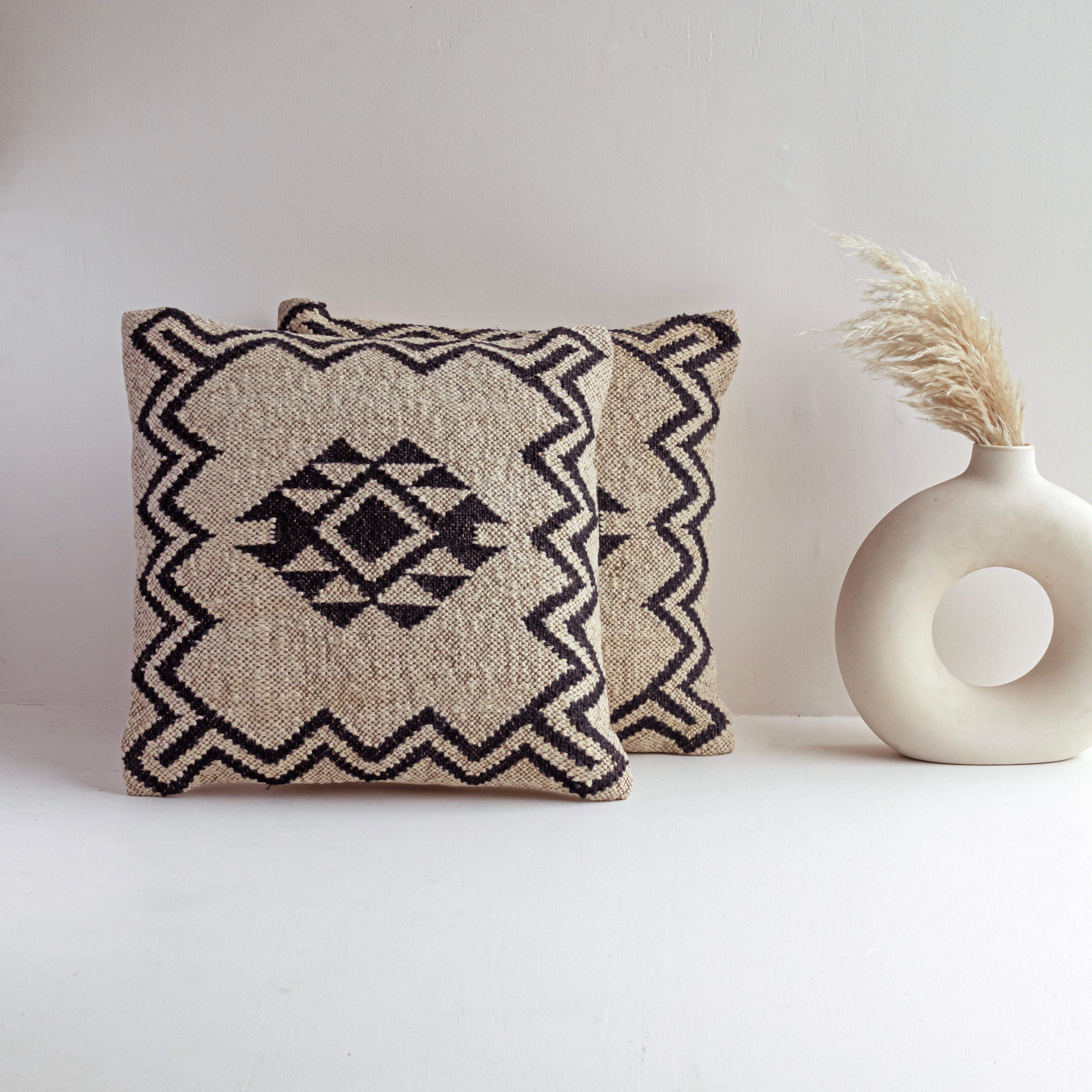 Handwoven black and ivory Kilim cushion cover featuring a geometric tribal diamond pattern displayed in a modern minimalist home setting.