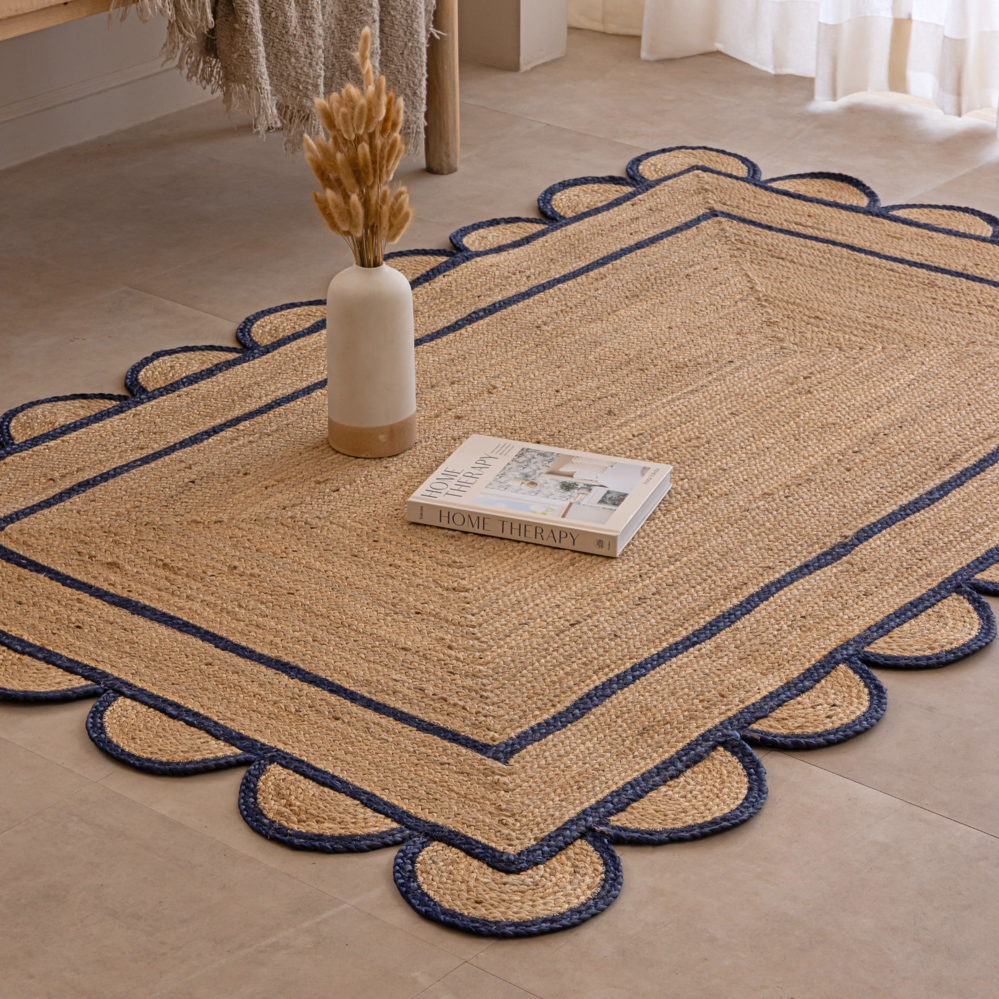 Handmade natural jute area rug with navy blue scalloped braided border in a cozy modern living room.