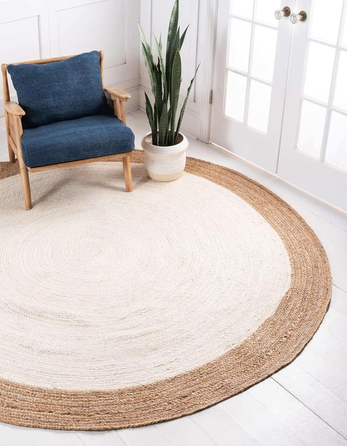 Handmade natural jute and ivory round rug with braided texture in a cozy neutral boho living room with a wooden coffee table and beige sofa.