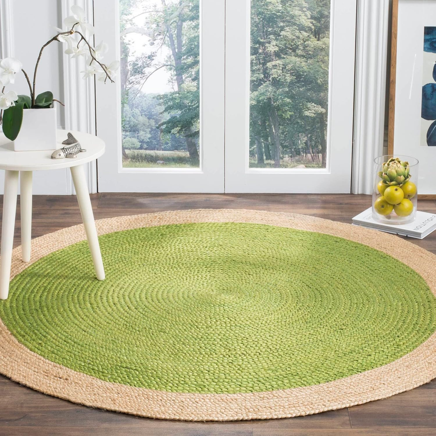Handmade green round braided jute rug with a natural beige border in a cozy modern living room, featuring a wooden coffee table, neutral sofa, and indoor plants.