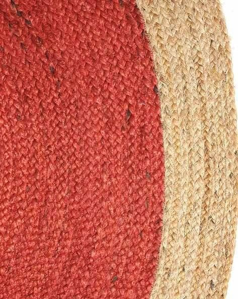 Handmade red round braided jute rug with a natural beige border, placed in a bright boho-style living room with indoor plants and wooden flooring.